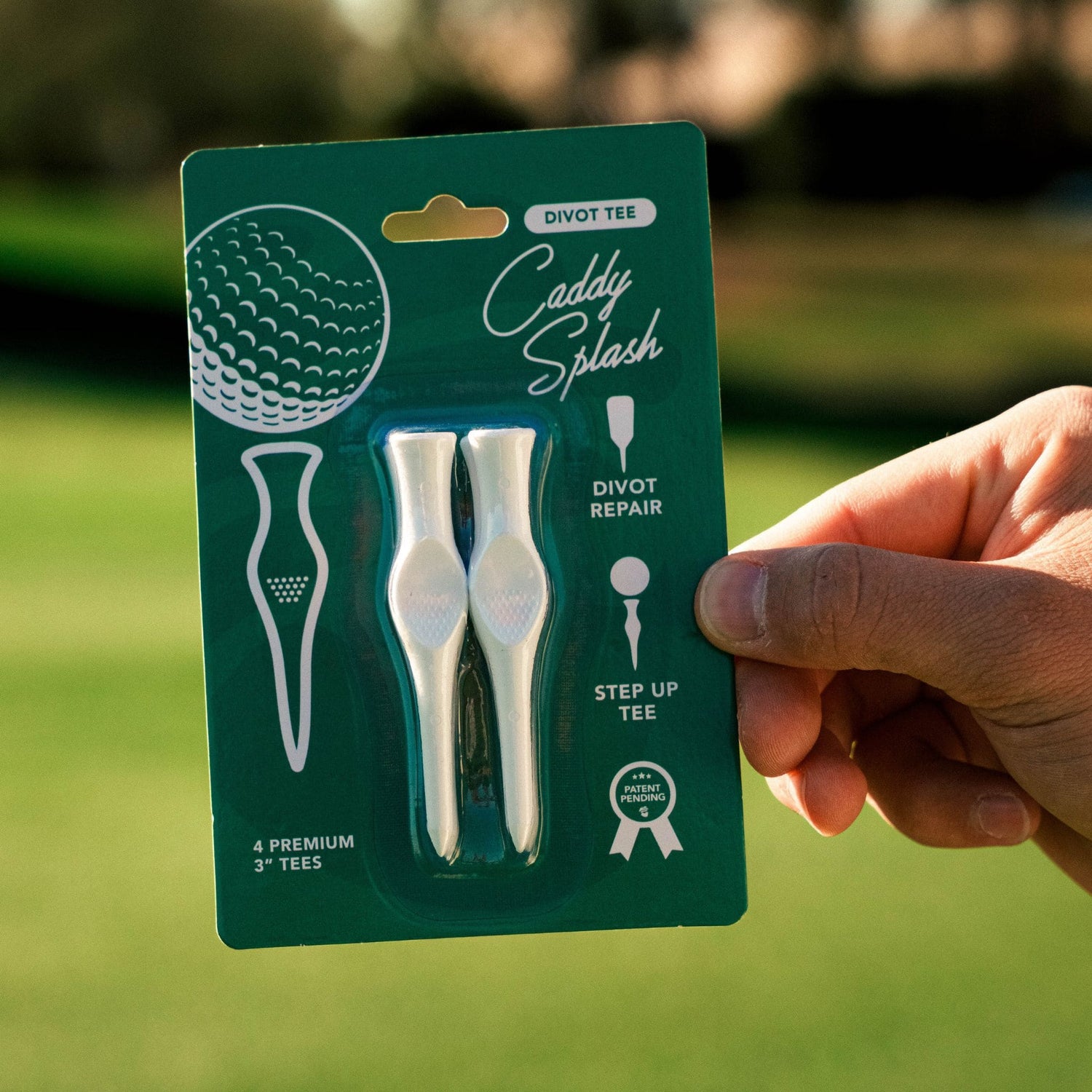 Caddy Splash golf divot repair tool set in packaging held by a hand on a golf course background