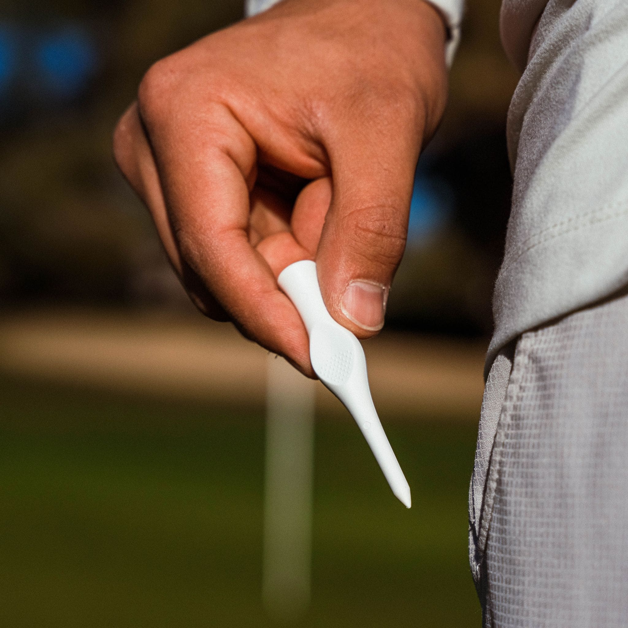 Hand holding a white golf tee with a blurred outdoor background