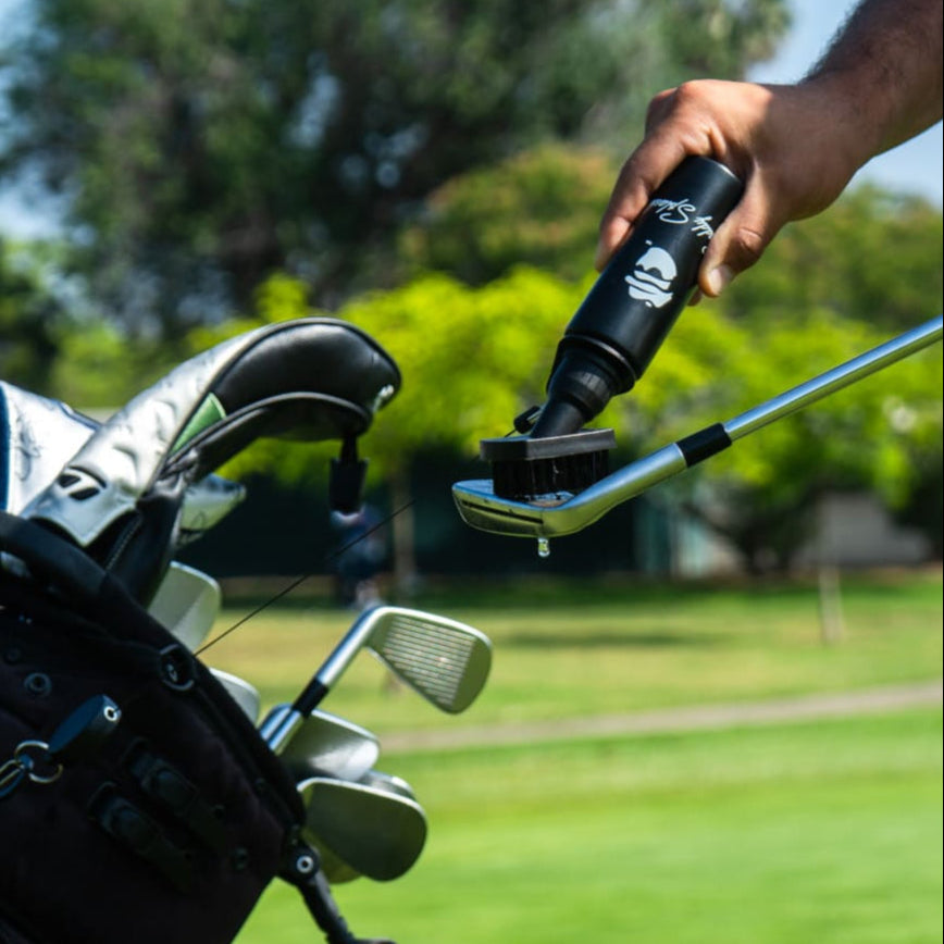 Person cleaning a golf club with a brush on a golf course