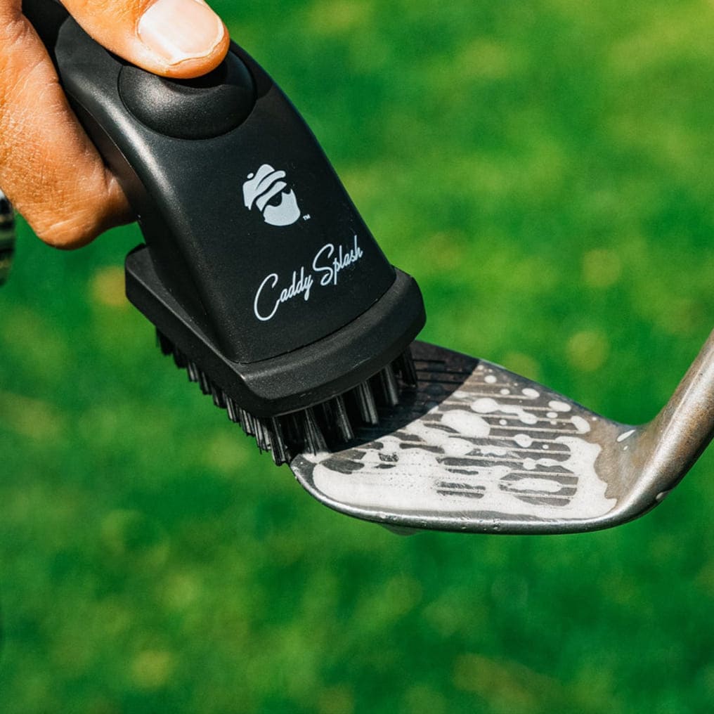Golf club being cleaned with a Caddy Shack brush against a green background
